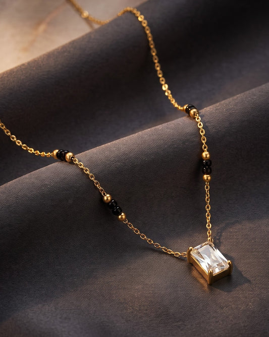 Solreya Baguette Solitaire Mangalsutra — a bezel-set baguette cubic zirconia solitaire on gold-tone chain with black beads, hero shot, laid flat