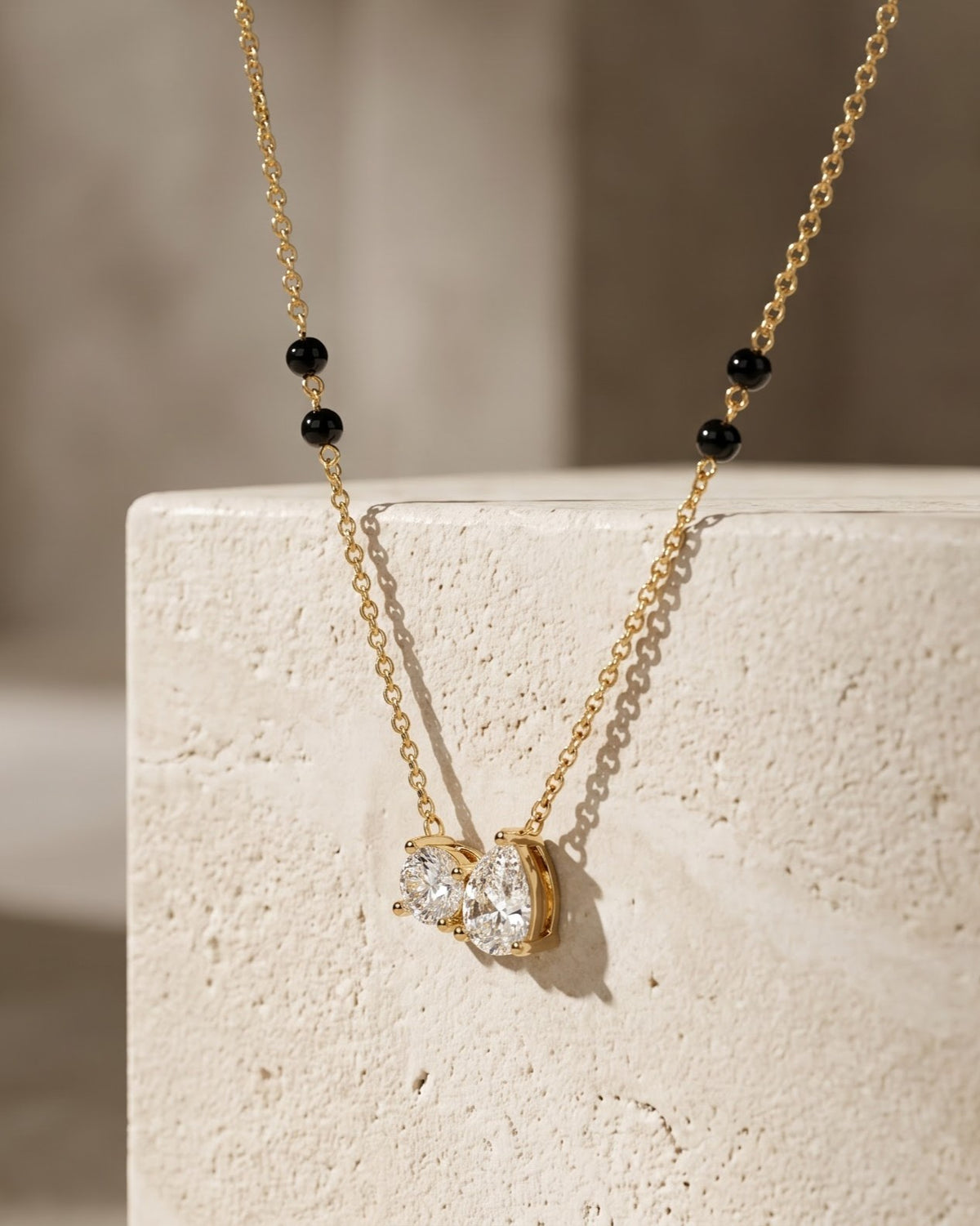 Solveya Drop Duo Mangalsutra — a pear-cut and round-cut cubic zirconia duo on gold-tone chain with black beads, hero shot, laid flat