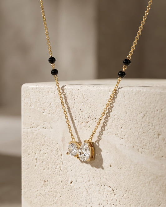 Solveya Drop Duo Mangalsutra — a pear-cut and round-cut cubic zirconia duo on gold-tone chain with black beads, hero shot, laid flat