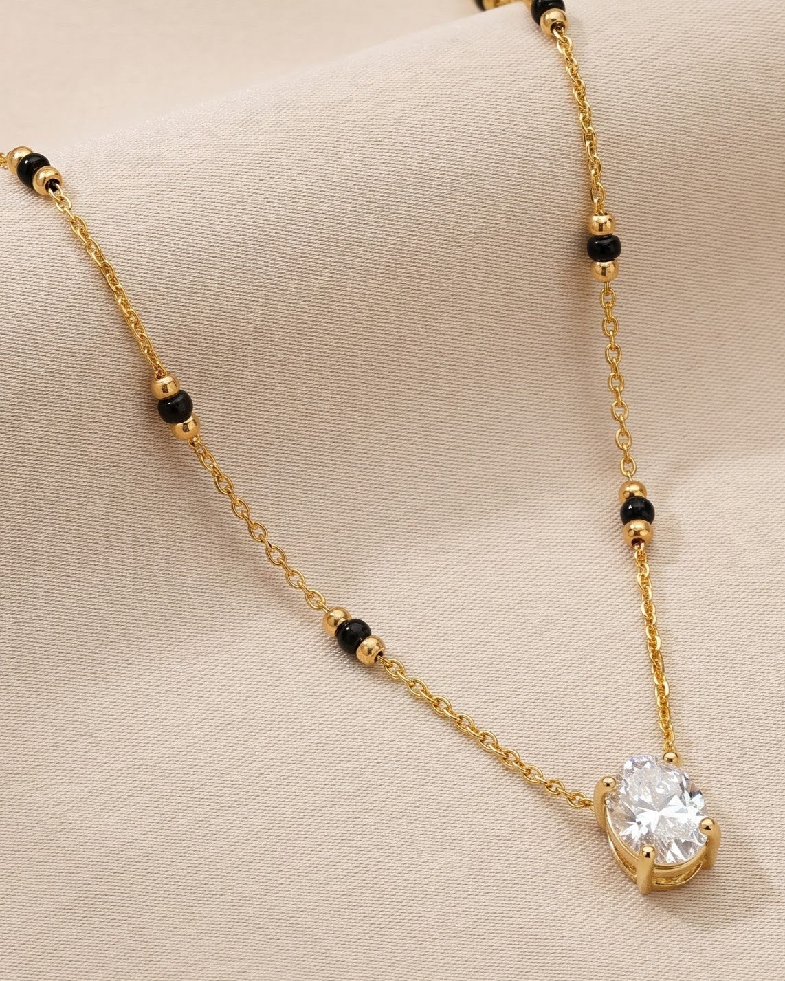 Solyne Oval Solitaire Mangalsutra — a bezel-set oval cubic zirconia solitaire on gold-tone chain with black beads, hero shot, laid flat